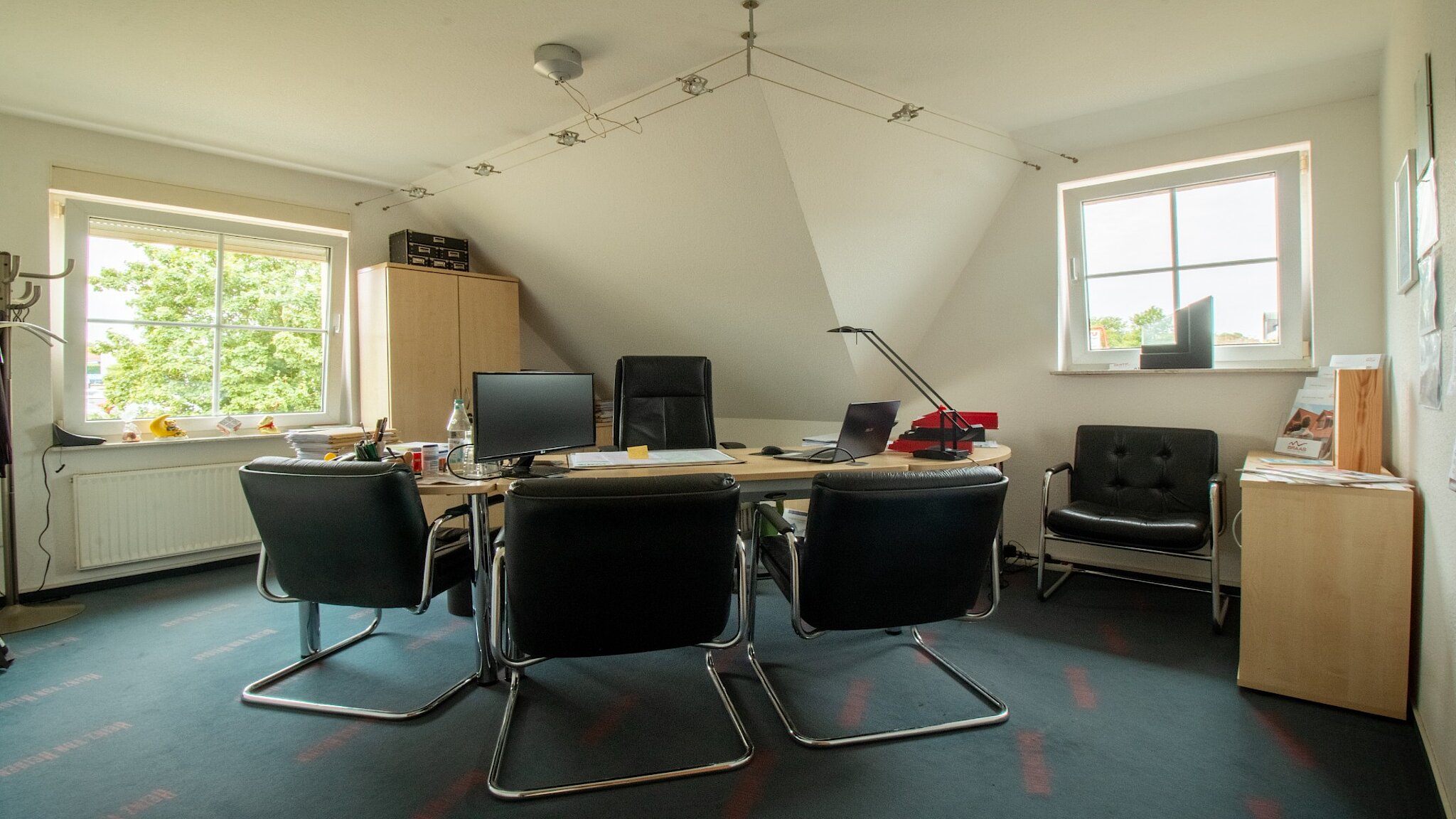 Beratungszimmer mit einem hellen Schreibtisch und drei Besucherstühlen. 