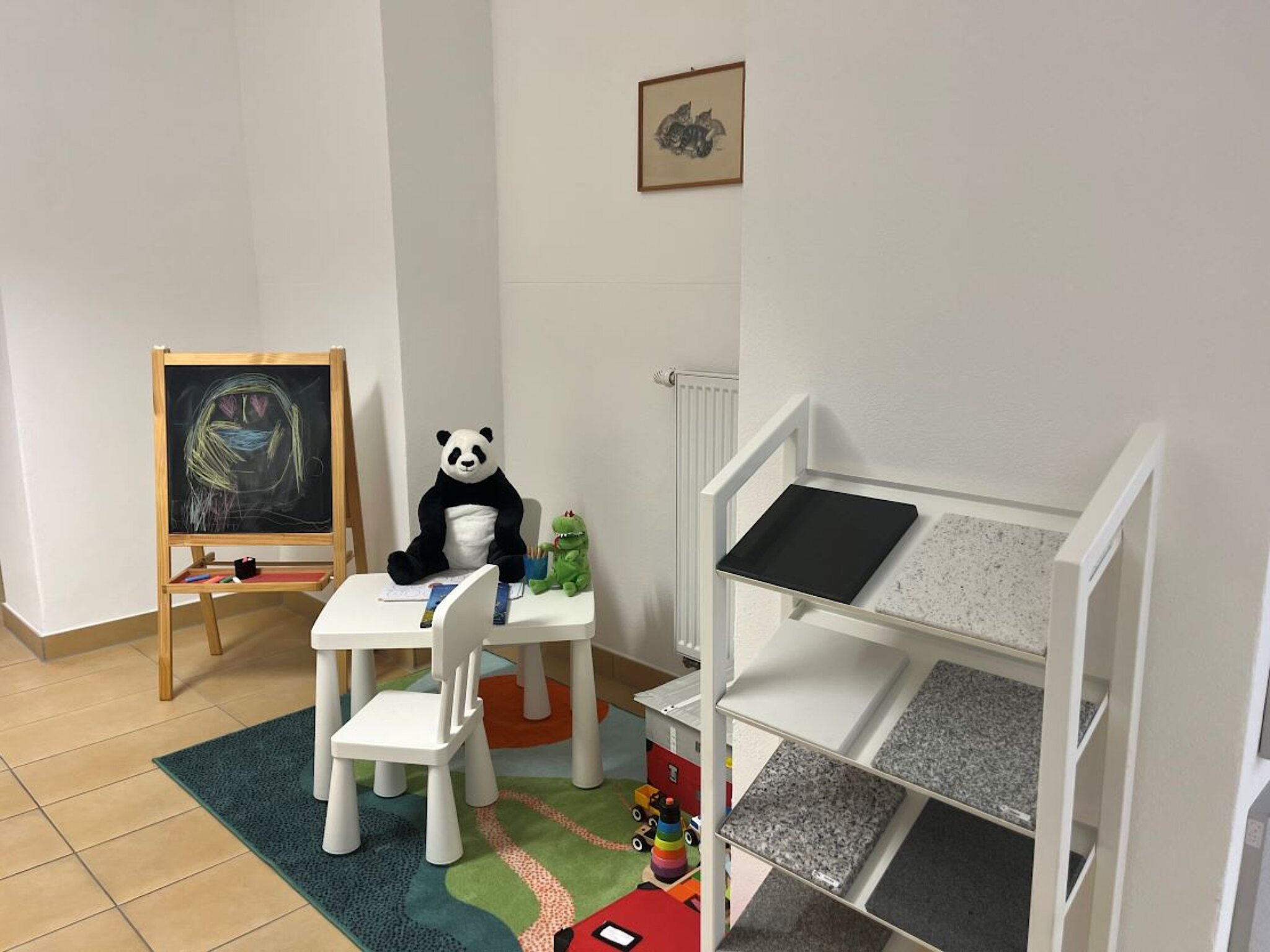 Spielecke mit buntem Teppich, verschiedenem Spielzeug und einer Maltafel.