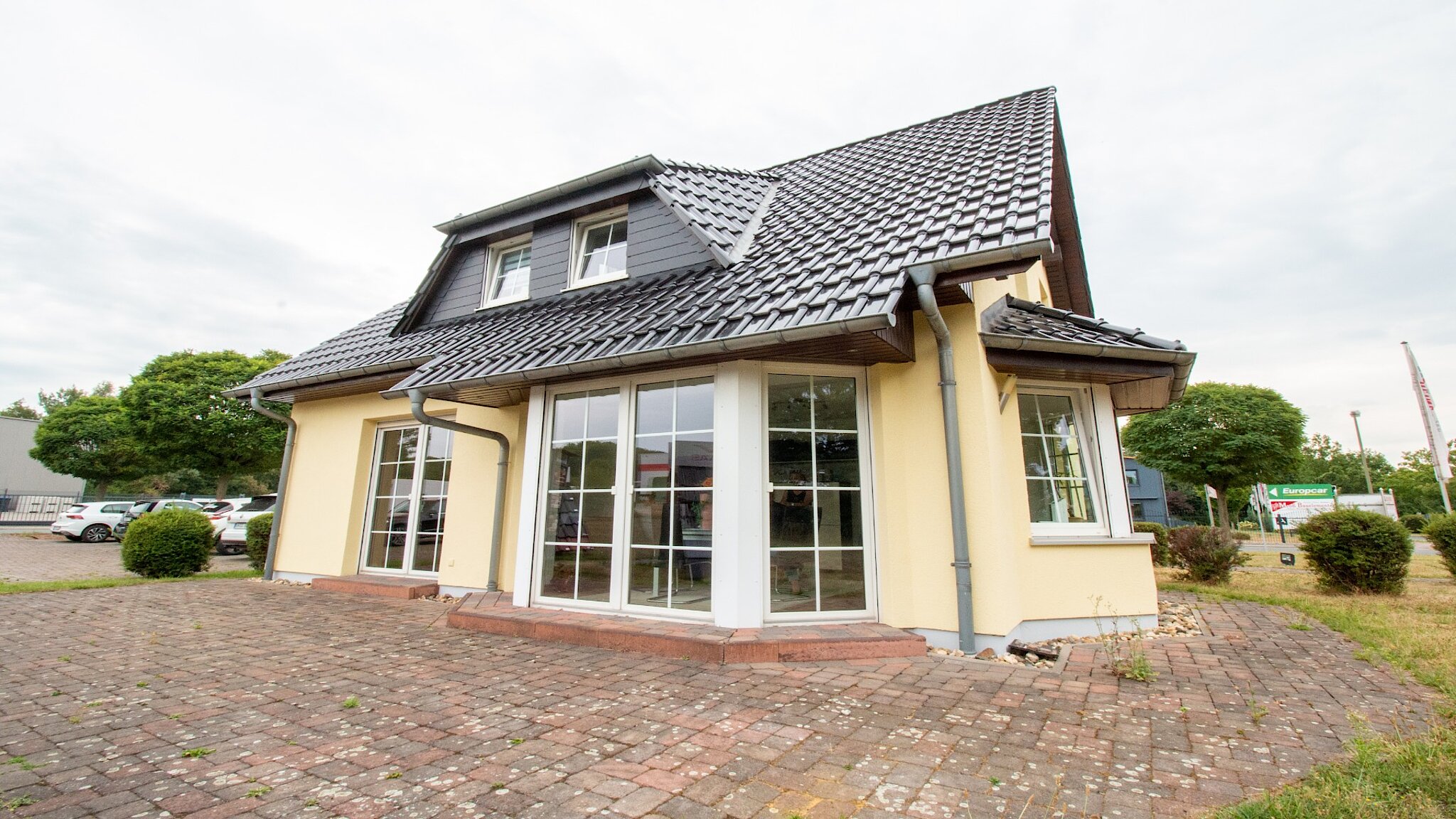 Außenansicht eines gelben Einfamilienhauses mit großer Fensterfront und Erker. 
