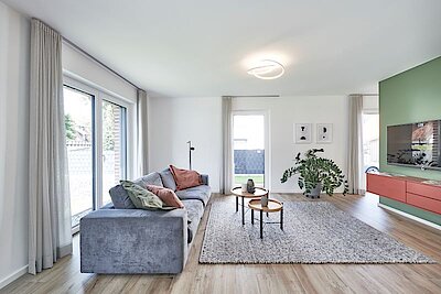 Helles Wohnzimmer mit blauer Couch, großem Teppich und TV. 