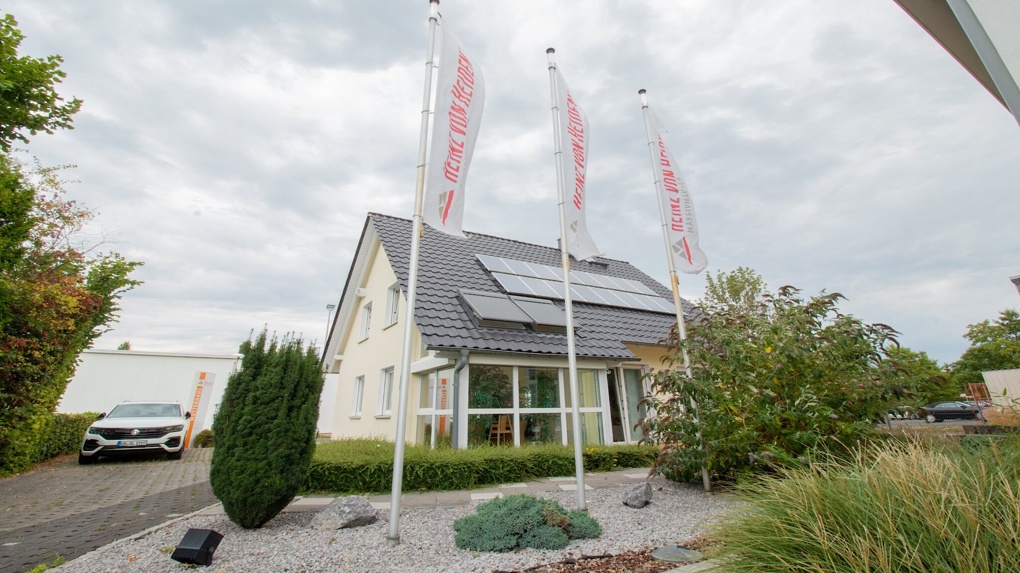 Außenansicht des Musterhauses Kamen mit drei Fahnenmasten im Vordergrund.